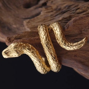 May include: A gold-coloured snake ring with a detailed, textured design. The snake is coiled and has a realistic head.