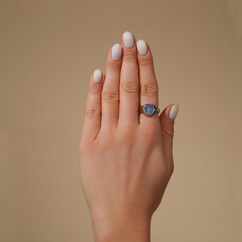 Op de afbeelding: Een zilveren ring met een blauwe ovale edelsteen. De ring zit aan een vinger.