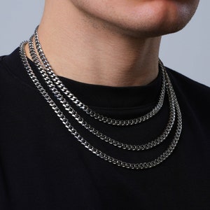 May include: Three silver curb chain necklaces layered on a person's neck. The chains are different lengths and widths.