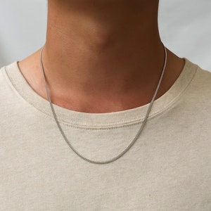 Könnte beinhalten: Eine silberne Kettenkette, die um den Hals einer Person getragen wird. Die Kette ist dünn und zart.