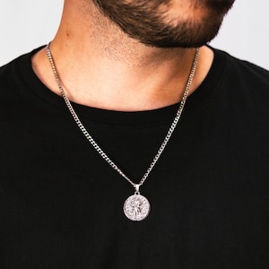 Könnte beinhalten: Eine silberne Kettenkette mit einem runden Anhänger mit einem detaillierten Design. Der Anhänger ist silberfarben und hat eine strukturierte Oberfläche.