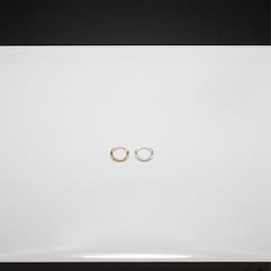 Puede incluir: Dos peque&ntilde;os pendientes de aro. Uno es de color dorado y el otro plateado. Ambos pendientes son circulares y parecen estar hechos de metal. Los pendientes se muestran sobre una superficie blanca.