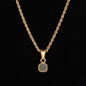 May include: Gold-toned necklace with a square pendant. The pendant has a dark blue-green center with gold flecks, set in a gold frame. The chain is a twisted rope design, and the background is black.