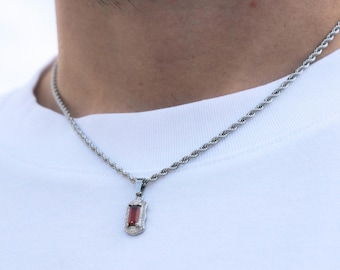 May include: Silver-toned rope chain necklace with a rectangular red gemstone pendant. The pendant is framed with small, clear accent stones. The necklace is worn against a white t-shirt.