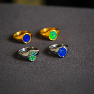 Op de afbeelding: Vier signet ringen met verschillende gekleurde opaalstenen. Twee ringen zijn zilver en twee zijn goud.