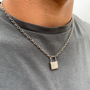 Puede incluir: Un collar de cadena de plata con un colgante de candado de plata.