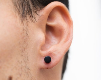 May include: A close-up of a person's ear with a black stud earring.