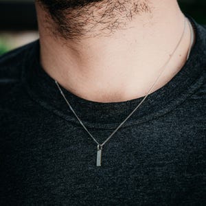 Op de afbeelding: Een zilveren ketting met een klein, rechthoekig hangertje.