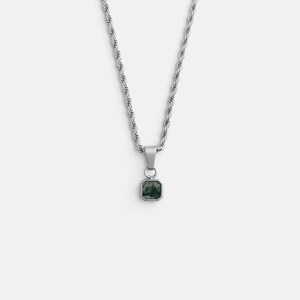 May include: A silver-toned necklace with a square pendant. The pendant features a dark green stone set in a silver frame. The chain is a twisted rope design. The necklace is displayed against a white background.