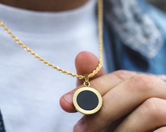 May include: A gold chain necklace with a round pendant featuring a black center and a gold rim. The pendant has a textured, ridged design.
