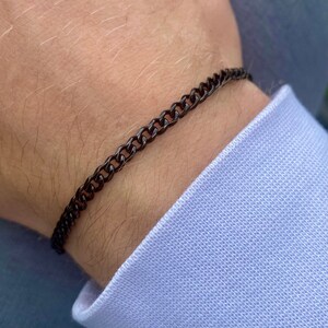 May include: A black chain bracelet on a person's wrist.