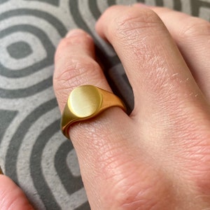 May include: A gold signet ring with a smooth, oval-shaped top.
