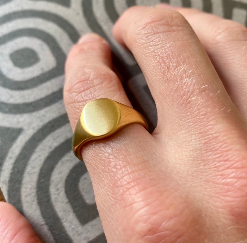 May include: A gold signet ring with a smooth, oval-shaped top.