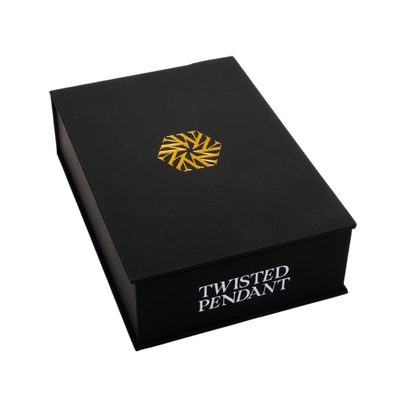 May include: A black rectangular box with a gold geometric design on the lid. The words "TWISTED PENDANT" are printed in white on the front of the box. The box is closed and appears to be made of cardboard.