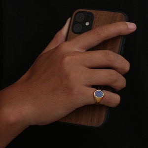 An 18K Gold Signet ring on Pink finger, Worn by a man holding a phone. The ring has a Lapis Lazuli stone in the centre