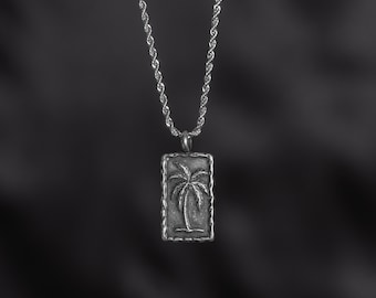 May include: A silver chain necklace with a rectangular pendant featuring an engraved palm tree.