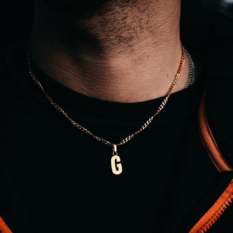 May include: A gold chain necklace with a gold pendant in the shape of the letter G.