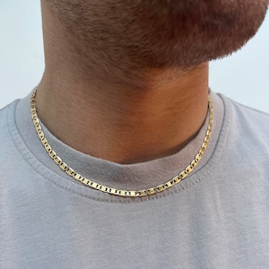 Może przedstawiać: Złoty naszyjnik z łańcuszkiem w stylu marynarskim. Łańcuszek nosi osoba w jasnoszarym t-shircie.