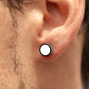 May include: A close-up of a person's ear with a white and black circular earring. The earring has a silver rim.