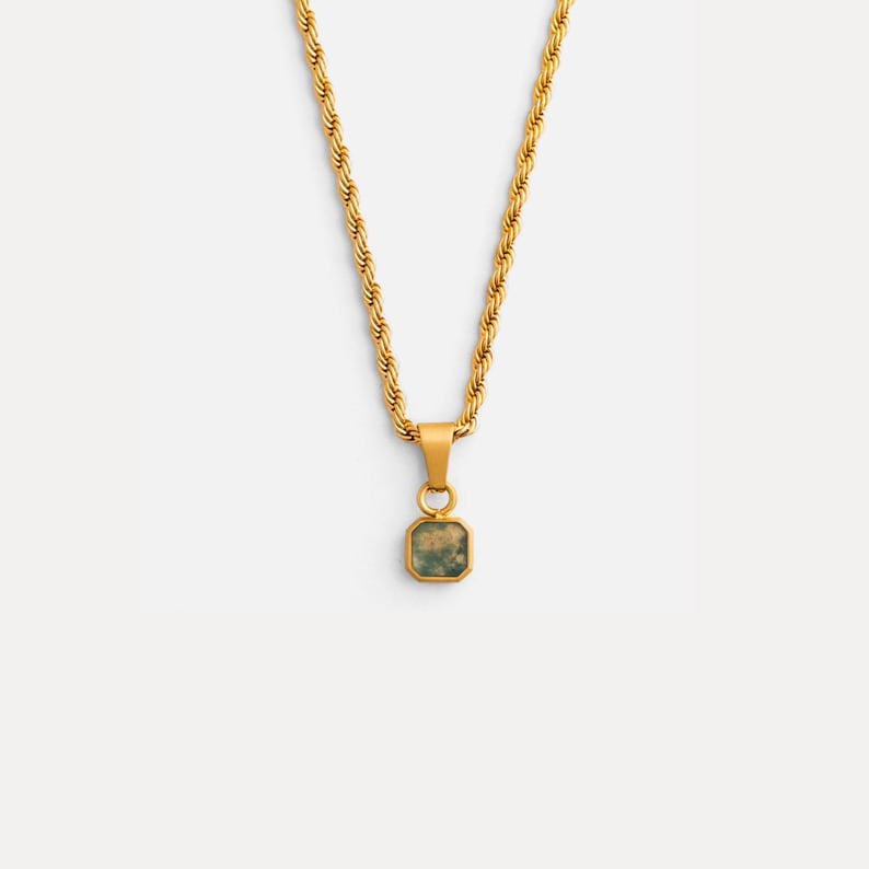 May include: Gold-toned necklace with a rope chain and a square pendant. The pendant features a light green stone with a mottled pattern. The necklace is displayed against a white background.