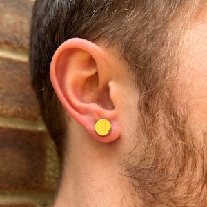 Könnte beinhalten: Nahaufnahme eines Ohres mit einem kleinen, runden, goldenen Ohrring. Der Ohrring ist schlicht und minimalistisch gestaltet.