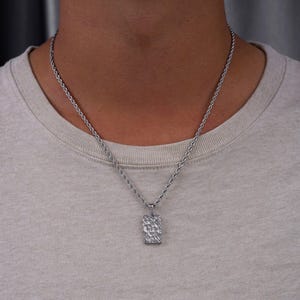Op de afbeelding: Een zilveren ketting met een getextureerde rechthoekige hanger.