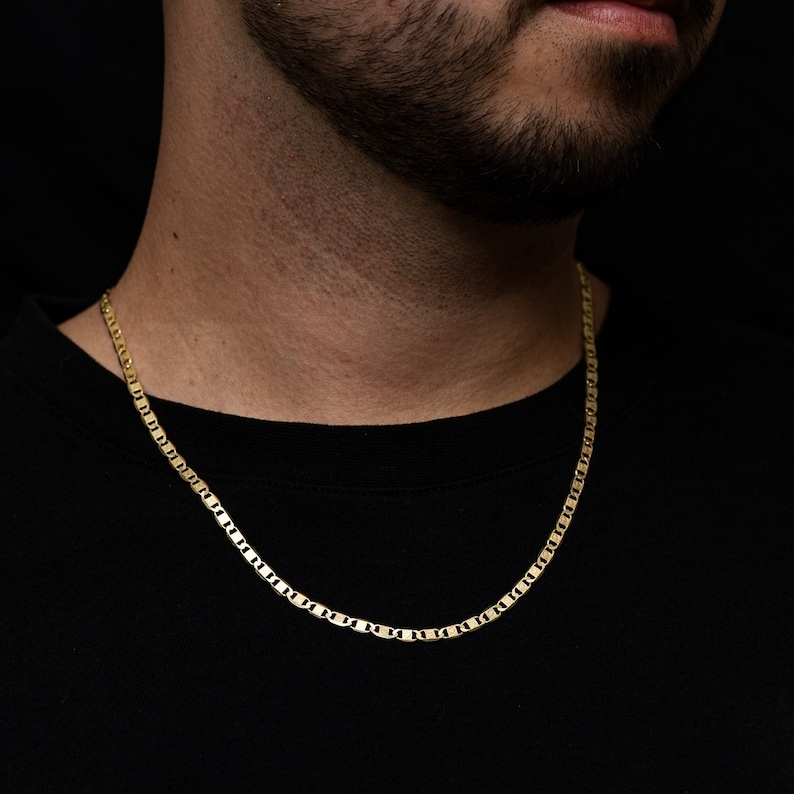 May include: A gold chain necklace with a mariner link style. The chain is worn by a person with a beard and a black shirt.