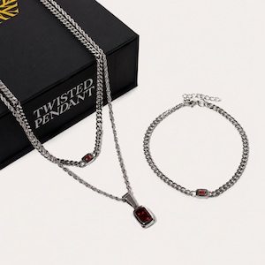 Pode incluir: Um conjunto de colar em camadas e pulseira a condizer em tom prateado. O colar apresenta uma corrente de corda e uma corrente de elos com um pendente retangular de pedra vermelha. A pulseira é uma corrente de elos com uma pedra vermelha.