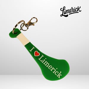 Könnte beinhalten: Grüner und weißer Schlüsselanhänger in Form eines Hurleys, ein traditioneller irischer Stock, der im Sport Hurling verwendet wird. Der Schlüsselanhänger hat ein rotes Herz und den Text "I Love Limerick" darauf.