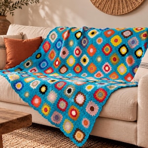 May include: A handmade crochet blanket featuring a vibrant turquoise blue base with a repeating pattern of multi-colored granny squares. Each square contains a central color surrounded by white and turquoise borders, creating a textured, geometric design.