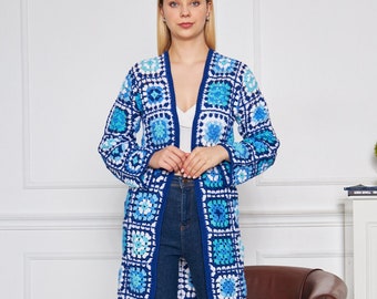 Puede incluir: Un cárdigan largo de crochet azul y blanco con un patrón de cuadrados de la abuela. El cárdigan está abierto en la parte delantera y tiene mangas largas. La modelo lleva pantalones vaqueros azules y zapatillas blancas.
