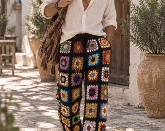 Puede incluir: Pantalones largos con base negra y un colorido patrón de ganchillo granny square en tonos rojo, azul, amarillo y blanco. Los pantalones tienen cintura con cordón y corte recto, combinados con una camisa de botones de color beige claro.