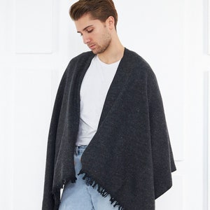 May include: A charcoal gray shawl with fringed edges. The shawl is draped over a person wearing a white t-shirt and light blue jeans.