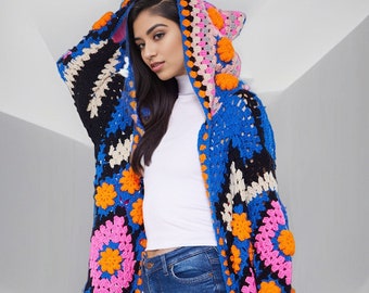 May include: A long, colourful crochet cardigan with a hood. The cardigan is made of a variety of colours, including blue, pink, orange, and black. The cardigan has a crocheted pattern with large squares and flowers. The cardigan is worn over a white turtleneck shirt and blue jeans.