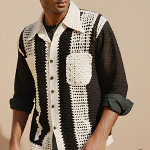 May include: A black and white crocheted long-sleeved shirt with a button-up front and a patch pocket on the left side.