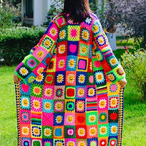 Puede incluir: Una colorida chaqueta de ganchillo con un diseño de patchwork que presenta caras sonrientes. La chaqueta está hecha de una variedad de colores brillantes, incluyendo rosa, azul, verde, amarillo y rojo. La chaqueta es de estilo largo y holgado y tiene un ajuste relajado.