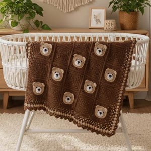 May include: A dark brown crochet baby blanket featuring a repeating pattern of small, light brown and white bear faces. The blanket has a decorative scalloped border in a lighter tan shade and is draped over a white oval-shaped baby crib.