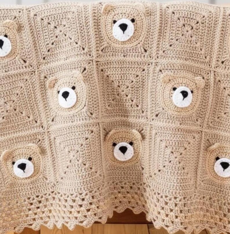 May include: A beige crochet blanket composed of square panels featuring three-dimensional bear faces. Each bear face is crafted with a white muzzle, black embroidered nose, and small rounded ears. The blanket edge has a decorative scalloped border.