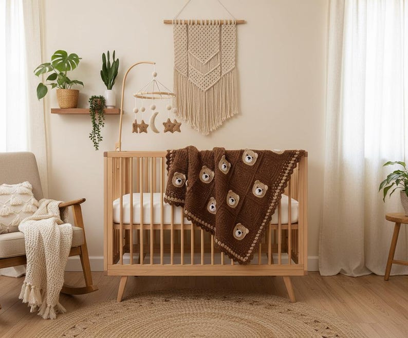 May include: A dark brown crochet baby blanket featuring a repeating pattern of square patches, each adorned with a small, light brown bear face appliqu&eacute;. The blanket has a decorative scalloped border and is draped over a light wood slatted crib.