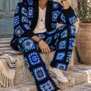 Puede incluir: Un conjunto de c&aacute;rdigan y pantal&oacute;n de ganchillo con base negra y motivos de cuadrados de la abuela en azul vibrante, azul claro y morado. El c&aacute;rdigan tiene cuello y pu&ntilde;os de canal&eacute; negro, combinado con zapatillas de lona blancas.