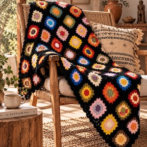 Può includere: Una coperta all'uncinetto fatta a mano con un classico motivo a piastrelle granny. Il design è composto da numerosi piccoli quadrati multicolori nelle tonalità del rosso, giallo, blu, rosa e verde, uniti da un bordo in filato nero.