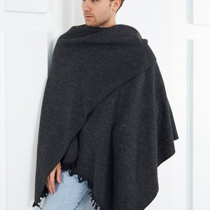 May include: A dark gray shawl with a fringed edge. The shawl is draped over a person's shoulders and is worn with light blue jeans.