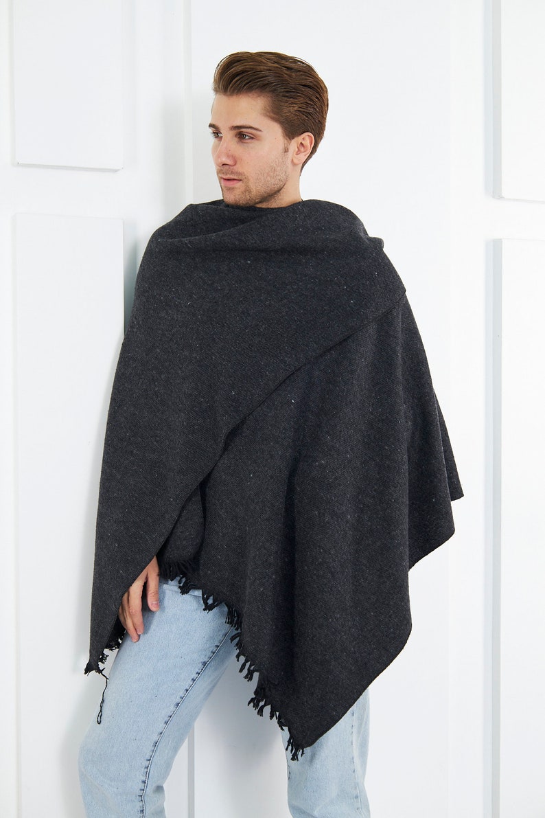 May include: A dark gray shawl with a fringed edge. The shawl is draped over a person's shoulders and is worn with light blue jeans.