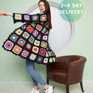 May include: A woman wearing a colorful crochet cardigan with a black background and a geometric pattern. She is standing in front of a light green wall and a brown chair. The text "2-4 DAY DELIVERY" is visible in the upper right corner of the image. The text "READY TO SHIP!" is visible in the lower center of the image.