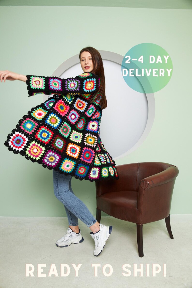May include: A woman wearing a colorful crochet cardigan with a black background and a geometric pattern. She is standing in front of a light green wall and a brown chair. The text "2-4 DAY DELIVERY" is visible in the upper right corner of the image. The text "READY TO SHIP!" is visible in the lower center of the image.