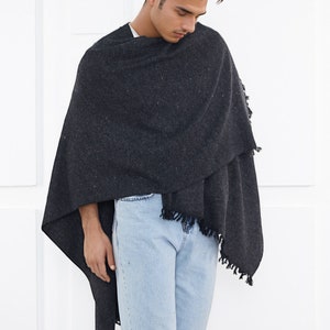 May include: A person wearing a dark gray shawl with a fringe trim over a white shirt and light blue jeans.