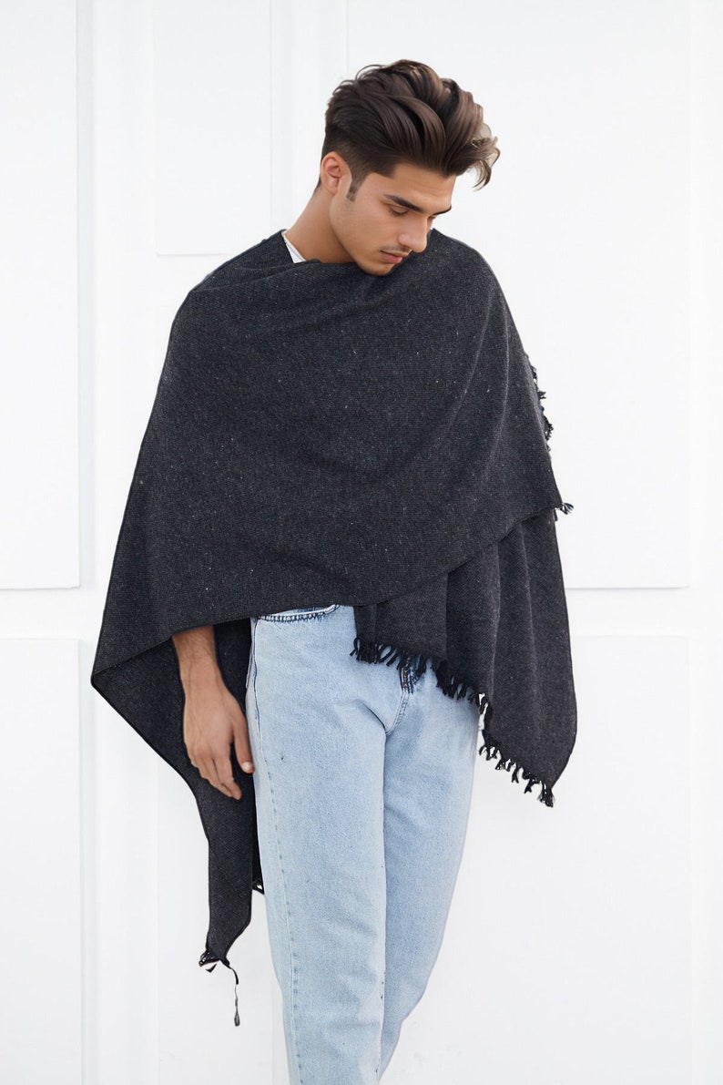 May include: A person wearing a dark gray shawl with a fringe trim over a white shirt and light blue jeans.