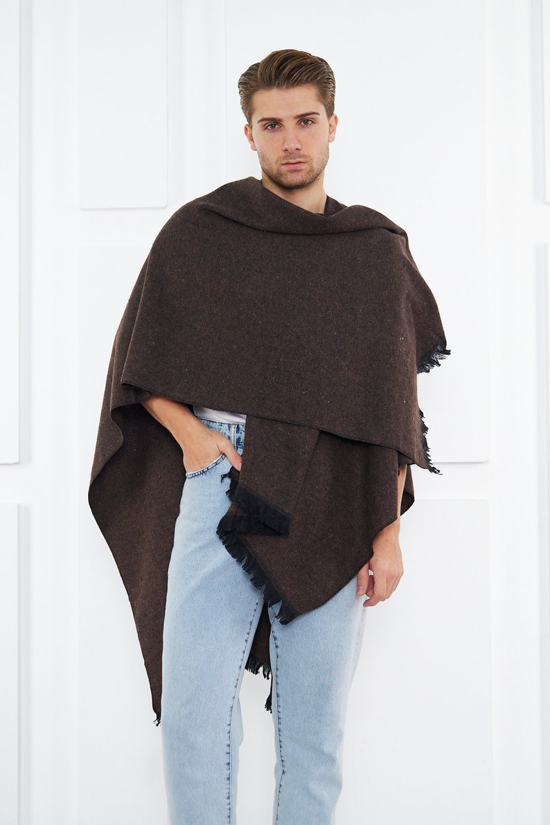 May include: A brown fringed shawl with a textured pattern. The shawl is draped around a person's shoulders and is worn with light blue jeans.