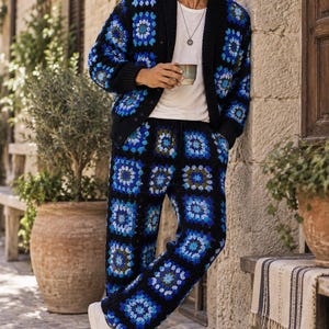 Puede incluir: Un conjunto de c&aacute;rdigan y pantalones de ganchillo con base negra y motivos de cuadrados de la abuela en azul, azul claro y verde oscuro. El c&aacute;rdigan tiene cierre de botones y pu&ntilde;os acanalados, mientras que el pantal&oacute;n tiene cintura con cord&oacute;n.