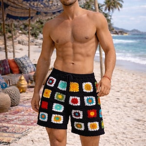 May include: Black crochet shorts with colorful square patterns. The shorts feature a drawstring waist and are worn on a sandy beach. The squares have red, yellow, blue, and white accents.
